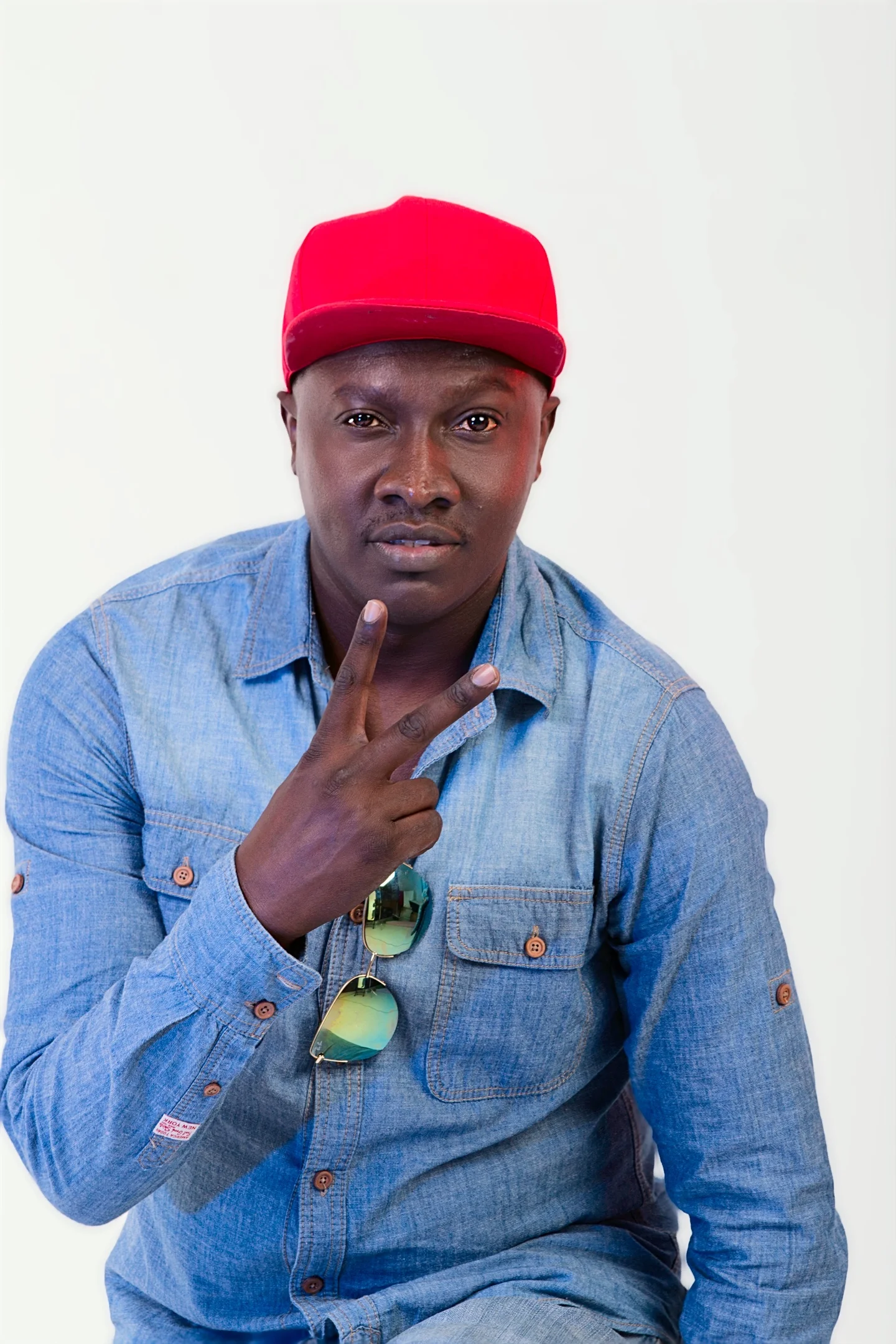 Muzikal Sheriff in a denim shirt and red cap, making a peace sign.