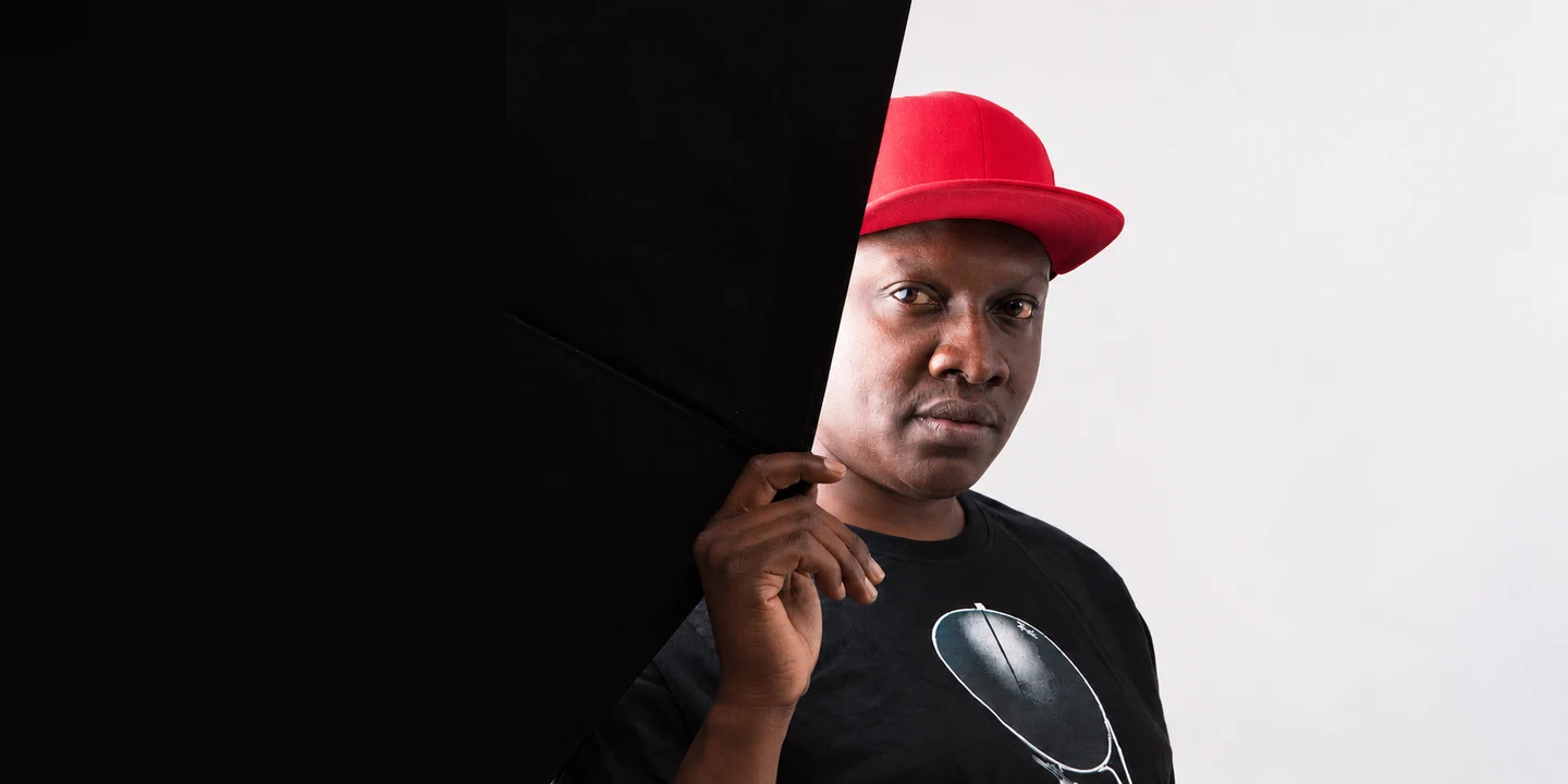 Muzikal Sheriff in a red cap beside a dark curtain.