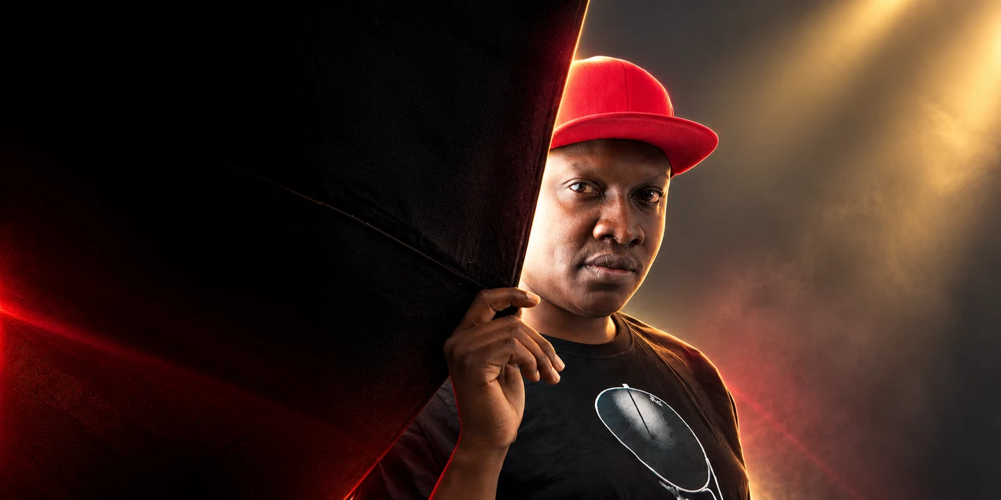 Muzikal Sheriff in a red cap beside a dark curtain, with warm golden lighting.