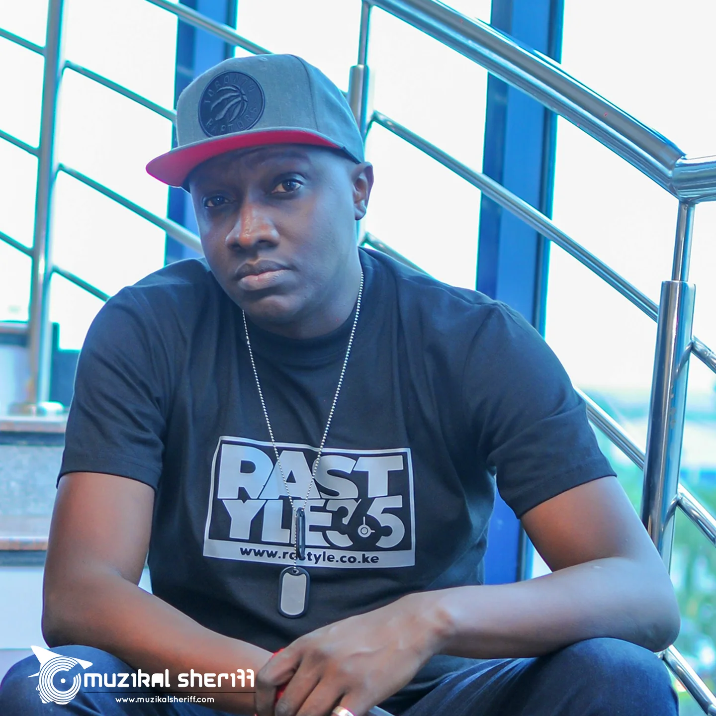 Muzikal Sheriff seated beside a staircase wearing a Rastyle T-shirt.