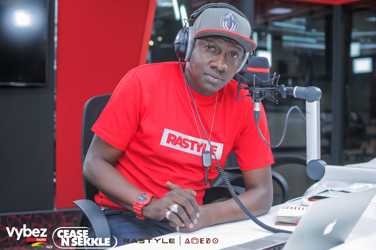 Muzikal Sheriff seated at a microphone in a Vybez Radio studio, with Cease N Sekkle branding.